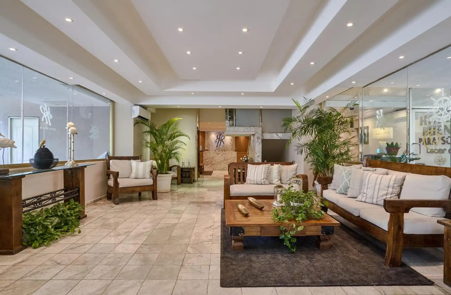 Lobby tropical del Hotel Riazor en Santo Domingo, con palmas, suelos de mármol y mobiliario de madera